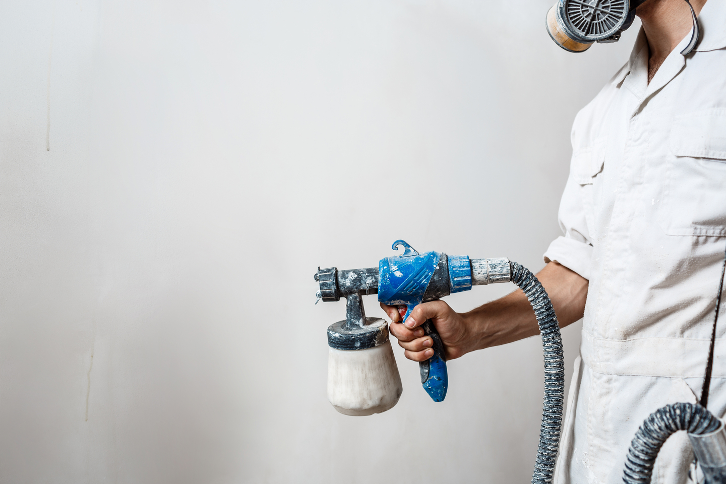 Worker painting wall with spray gun in white color. Copy space.