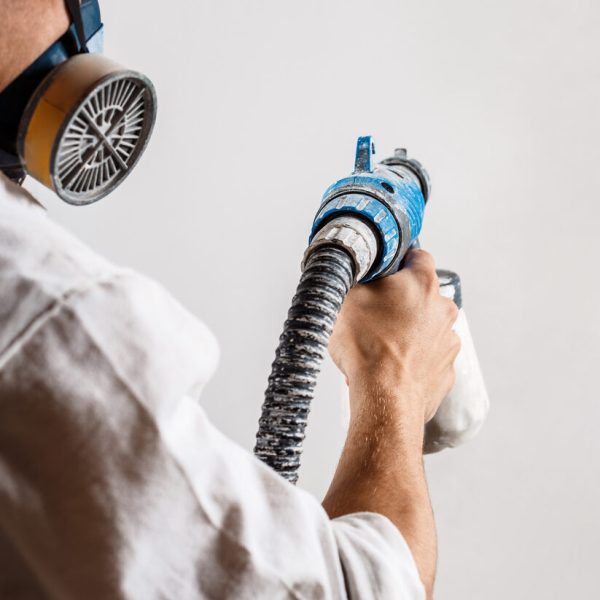 Worker painting wall with spray gun in white color. Copy space.